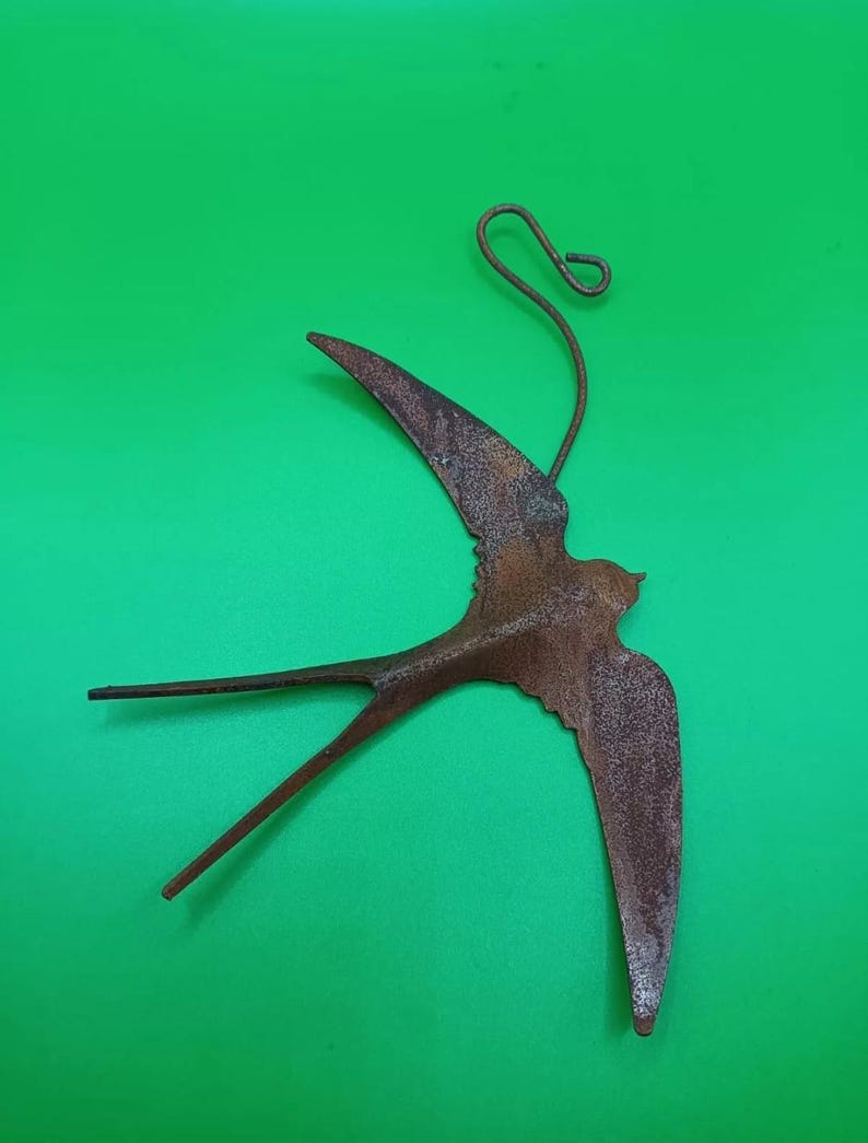 May include: A rusty metal swallow bird ornament with a loop for hanging. The bird is in flight with its wings spread out.