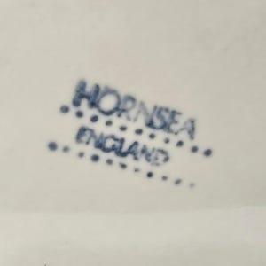 May include: Close-up of a white surface with the blue text "HORNSEA ENGLAND" printed on it. The text is arranged in two lines, with "HORNSEA" above "ENGLAND". The text is surrounded by small blue dots.
