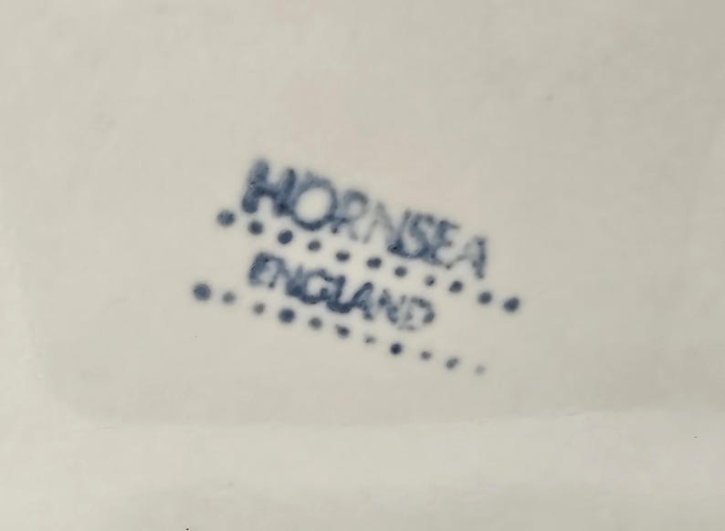 May include: Close-up of a white surface with the blue text "HORNSEA ENGLAND" printed on it. The text is arranged in two lines, with "HORNSEA" above "ENGLAND". The text is surrounded by small blue dots.