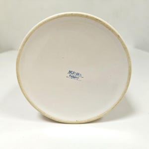 May include: A white ceramic vase with a slightly flared rim. The bottom of the vase features the text "HORNSEA ENGLAND" in blue. The vase has a simple, classic design.