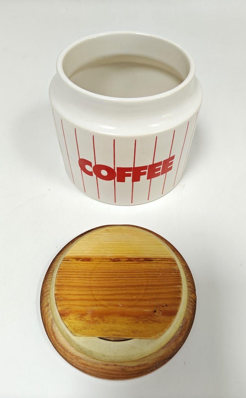 May include: A white ceramic mug with a black handle and the text "But First, Coffee" in a handwritten style. The mug is on a white surface. The mug is approximately 4 inches tall.