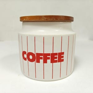 May include: A white ceramic coffee canister with a wooden lid. The canister has red vertical stripes and the word "COFFEE" in large red letters. A kitchen storage container.