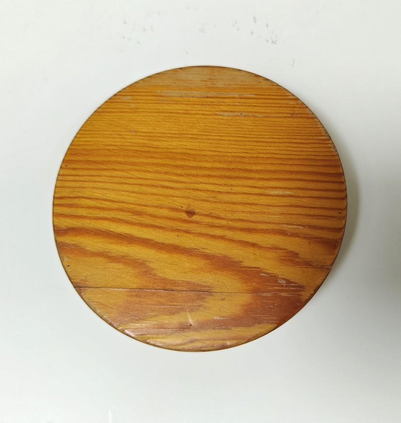 May include: A round wooden object with a light brown finish and visible wood grain. The object appears to be a lid or a coaster, with a diameter of approximately 8 inches.