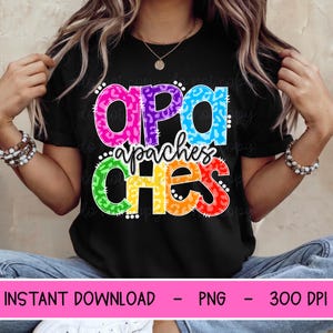May include: A black short-sleeved t-shirt featuring a multi-colored graphic print with the text "apaches" in a bold, leopard-spotted pattern. The letters are colored in pink, purple, blue, green, yellow, and red, with a script font overlay.