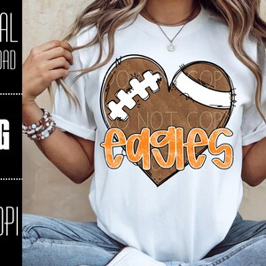 Puede incluir: Camiseta blanca con un dise&ntilde;o de f&uacute;tbol americano en forma de coraz&oacute;n y la palabra "Eagles" en naranja. El dise&ntilde;o incluye un bal&oacute;n de f&uacute;tbol marr&oacute;n con cordones blancos y una franja blanca. Tambi&eacute;n se ven las palabras "DIGITAL DOWNLOAD", "PNG" y "300 DPI".