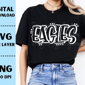 Op de afbeelding: Zwart T-shirt met het woord "EAGLES" in een witte, bubbelachtige letter. Het shirt wordt gedragen door een persoon in een spijkerbroek. De afbeelding bevat ook de tekst "DIGITALE DOWNLOAD", "SVG 1 & 2 LAAG" en "PNG 300 DPI".