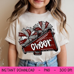 May include: A beige t-shirt featuring a maroon megaphone design with the word "Cheer" in white. The design includes gray and maroon pom-poms. The bottom of the image has the text "INSTANT DOWNLOAD - PNG - 300 DPI".