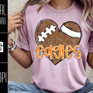 Puede incluir: Camiseta rosa claro con un dise&ntilde;o de coraz&oacute;n en forma de bal&oacute;n de f&uacute;tbol y la palabra "Eagles" en naranja. El coraz&oacute;n de f&uacute;tbol tiene detalles en blanco y marr&oacute;n. Las palabras "DIGITAL DOWNLOAD", "PNG" y "300 DPI" est&aacute;n en el lado izquierdo.