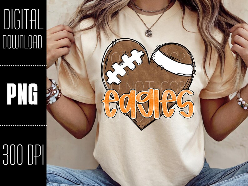 Puede incluir: Camiseta de color beige claro con un dise&ntilde;o de bal&oacute;n de f&uacute;tbol en forma de coraz&oacute;n y la palabra "Eagles" en naranja. El bal&oacute;n de f&uacute;tbol es marr&oacute;n con detalles blancos. Las palabras "DIGITAL DOWNLOAD", "PNG" y "300 DPI" est&aacute;n en el lado izquierdo.