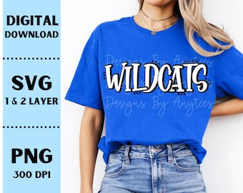 Könnte beinhalten: Ein königsblaues T-Shirt mit dem Wort "WILDCATS" in weißer, fetter Schrift mit schwarzer Umrandung. Das Shirt hat auch den Text "Designs By Anytees" in einer Schreibschrift. Das Bild enthält auch den Text "DIGITALER DOWNLOAD", "SVG 1 & 2 LAYER" und "PNG 300 DPI".