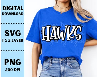 Op de afbeelding: Een koningsblauw t-shirt met het woord "HAWKS" in een vetgedrukte, witte letter met een zwarte omlijning. Het shirt toont ook de tekst "Designs By Anytees". Digitale downloadopties voor SVG- en PNG-bestanden worden ook getoond.