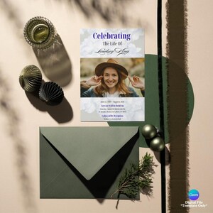 May include: A flat lay featuring a memorial card with the text "Celebrating The Life Of Lindsey King" and a photo of a woman. An envelope, decorative spheres, and a sprig of greenery are also present.