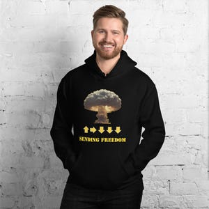 May include: Black hooded sweatshirt featuring a graphic of a mushroom cloud with yellow arrows and the text "SENDING FREEDOM". The design is centered on the front of the sweatshirt.