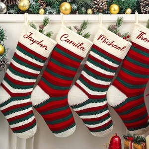 May include: Four Christmas stockings with names embroidered in red: Jayden, Camila, Michael, and Thomas. The stockings are red, green, and white striped with a white cuff and toe. Festive holiday decor.
