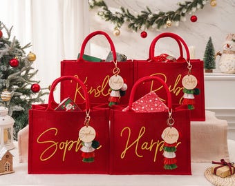 May include: Red tote bags with gold script names, each with a matching tassel keychain. The bags are filled with gifts and are decorated with Christmas-themed accessories. The bags have red handles.