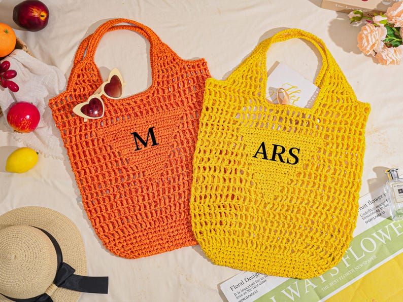 May include: Two open-weave crochet tote bags, one orange and one yellow, with large handles. The orange bag has the letter "M" and heart-shaped sunglasses. The yellow bag has the letters "ARS".