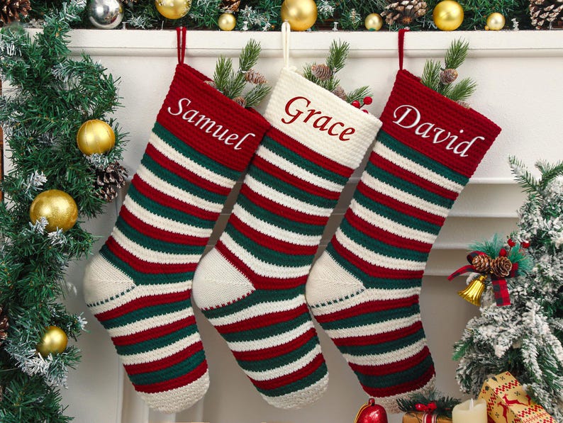 May include: Three personalized Christmas stockings with names embroidered in white. Each stocking features red, green, and white horizontal stripes. The names are Samuel, Grace, and David. The stockings are hanging in front of a decorated fireplace.