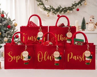 May include: Red tote bags with gold lettering, each personalized with a name. The bags have matching handles and are adorned with keychains featuring tassels and wooden name tags. The bags are filled with gifts and are decorated for Christmas.