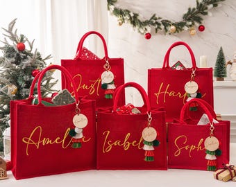 May include: Red jute tote bags with gold lettering and matching keychains. Each bag is personalized with a name: Amelia, Isabel, Harper, Sophia, and Justin. The bags have red handles and are decorated with tassels.