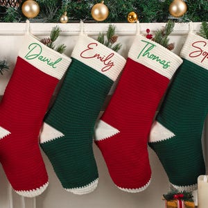 May include: Four personalized Christmas stockings in red and green, with white accents. Each stocking is embroidered with a name: David, Emily, Thomas, and Sophia. The stockings are hanging above a fireplace, decorated with ornaments and greenery.