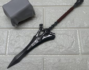 May include: A detailed, dark gray fantasy sword with a decorative hilt and a brown wrapped handle. The blade is long and pointed. A gray, cloth-covered object is in the background.