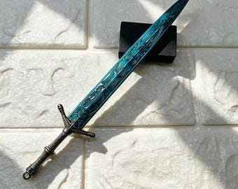 May include: A decorative sword featuring a metallic teal blade with intricate embossed swirling patterns and a dark grey, textured metal hilt. The sword has a pointed tip and a crossguard, with a small circular loop at the base of the handle.