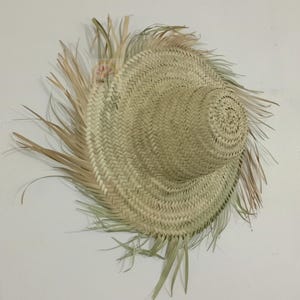 May include: A woven straw hat with a wide brim and a rounded crown. The hat is made of natural-colored straw and has a fringed edge. The hat is likely handmade and suitable for sun protection.