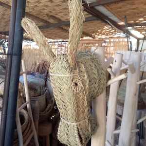 May include: A woven straw animal head sculpture, possibly a deer or goat, with long ears and a detailed face. The sculpture is brown and beige and has a natural, rustic look.