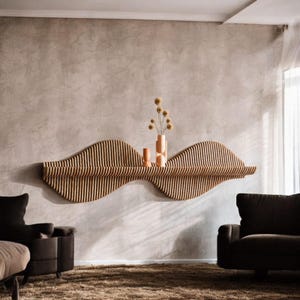 Puede incluir: Estantería de pared de madera ondulada con rayas verticales, que sostiene un jarrón y dos pequeños objetos decorativos. La estantería está montada en una pared de tono neutro, creando una estética moderna. La estantería mide unos 152 cm de ancho.