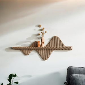Puede incluir: Estante de pared de madera con un diseño en forma de onda, con listones verticales. El estante contiene dos pequeños jarrones con flores secas. La paleta de colores es neutra, con madera marrón claro y un fondo de pared blanco. Un artículo de decoración del hogar moderno y minimalista.