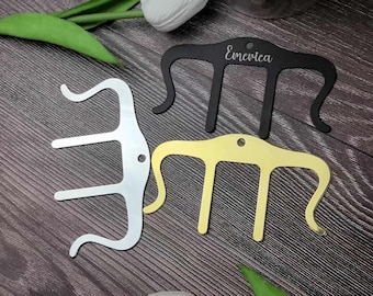 Puede incluir: Tres pinzas para el pelo de metal en diferentes acabados: plata, oro y negro. La pinza negra tiene la palabra "Emewica" grabada.