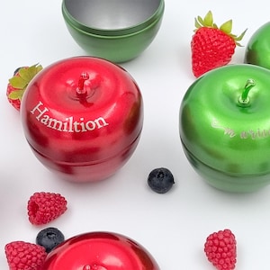 Puede incluir: Contenedores rojos y verdes en forma de manzana con tapas, algunos con texto. Los contenedores rojos tienen la palabra "Hamilton". Los contenedores verdes tienen la palabra "married". Bayas y otros contenedores están dispersos.