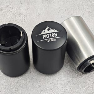 May include: Three bottle opener components. Two black cylindrical pieces and one silver cylindrical piece. The black piece in the centre has the word "PATTON" and "EST.2026" printed on it, with a mountain graphic.