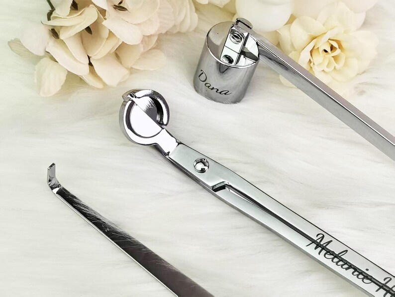 Op de afbeelding: Zilveren kaarsenaccessoireset, inclusief een lonttrimmer, een lontdompelaar en een kaarsensnuffer. De lonttrimmer en snuffer zijn gegraveerd met namen. Gepresenteerd op een witte, zachte ondergrond.