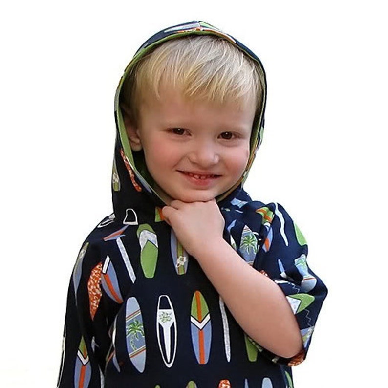 May include: A young child wearing a blue hooded sweatshirt with a colourful surfboard print. The sweatshirt has a green hood and a white drawstring.