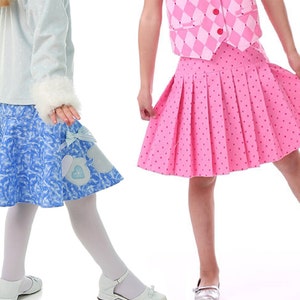 May include: Two girls wearing skirts. The girl on the left is wearing a light blue skirt with a white and blue pattern and a white bow. The girl on the right is wearing a pink skirt with white polka dots.