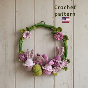 Può includere: Una ghirlanda pasquale all'uncinetto fatta a mano con una base di vite verde adornata con fiori rosa e viola, foglie verdi e coniglietti e uova all'uncinetto. Il testo "Crochet pattern" è visibile nell'immagine.