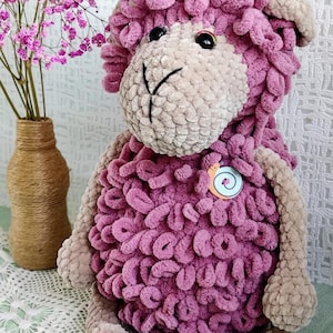 Op de afbeelding: Een handgemaakt schapenknuffel in roze en beige. Het schaap heeft een getextureerd lichaam, een lichtbeige gezicht en zwarte knoopogen. De afbeelding bevat de tekst "Crochet Pattern PDF".