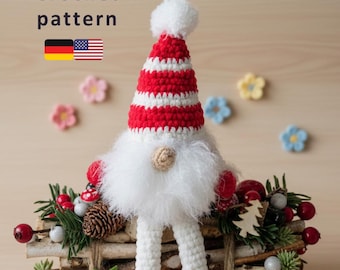 Op de afbeelding: Een handgemaakte gehaakte kabouter met een rood-wit gestreepte hoed, witte baard en rode laarzen. De kabouter is versierd met een feestelijk arrangement van bessen, dennenappels en groen. De tekst "Crochet pattern" is zichtbaar.