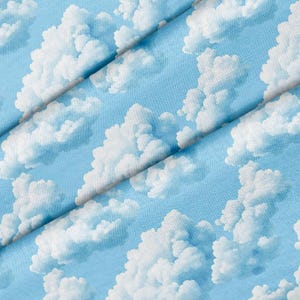 May include: Light blue fabric with a repeating pattern of fluffy white clouds. The clouds are painted with soft shading, creating a realistic sky effect. The fabric is folded, showing the texture and drape of the material.