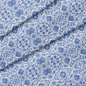 Könnte beinhalten: Ein Stoff mit einem sich wiederholenden Muster aus blauen Blumenmotiven und verschlungenen Ranken auf einem klaren weißen Hintergrund. Das Design zeigt eine dichte Anordnung von Blüten und Blättern, die eine durchgehende, symmetrische Textur erzeugt.