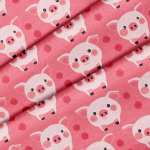 Può includere: Tessuto rosa con un motivo ripetuto di maiali dei cartoni animati e pois rossi. I maiali sono bianchi con orecchie, guance e musi rosa. Il tessuto è piegato, mostrando il motivo da diverse angolazioni.