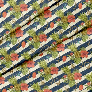 Op de afbeelding: Stof met een tropisch patroon met ananassen, hibiscusbloemen en mango's op diagonale strepen in marineblauw en wit. Het ontwerp bevat kolibries, touwen en kompasdetails.