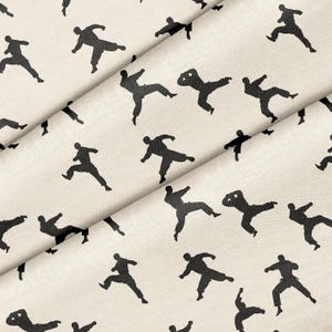 Könnte beinhalten: Cremefarbener Stoff mit einem sich wiederholenden Muster aus schwarzen Silhouetten von Menschen in dynamischen Posen. Der Stoff ist gefaltet und zeigt seine Textur und seinen Fall. Das Design ist einfach und grafisch.