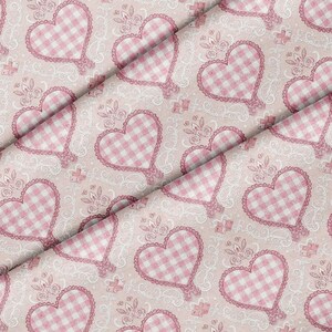 May include: Pink fabric with a repeating pattern of gingham hearts outlined with lace. The hearts are set against a pale pink background with a delicate floral and scroll design. A charming and romantic textile.