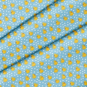 May include: Pale blue fabric featuring a repeating pattern of yellow cartoon ducks and small white polka dots. The fabric is folded, showing the texture and design. Suitable for baby or children's crafts.