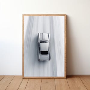 May include: A silver classic car driving on a snowy road. The car is viewed from above, with the road stretching out in front of it.