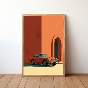 Puede incluir: Impresión artística enmarcada que presenta un coche deportivo naranja vintage estacionado frente a un edificio naranja con una puerta arqueada. El coche tiene detalles plateados y está sobre un fondo minimalista. La obra de arte está en un marco de madera.