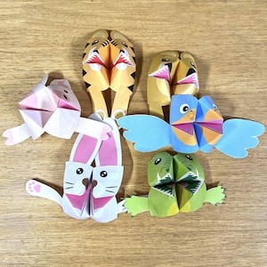 Può includere: Cinque giocattoli di animali di carta colorati con la bocca aperta. Gli animali sono una tigre, un coniglio, un uccello, un coccodrilo e un orso. Ogni animale è fatto di carta e ha un colore e un design diverso.