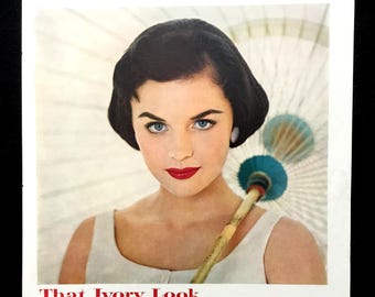 May include: Vintage advertisement featuring a woman with dark hair, blue eyes, and red lipstick. The ad promotes "That Ivory Look" with text emphasizing clarity and freshness. Includes a small image of a baby and a box of Ivory soap.